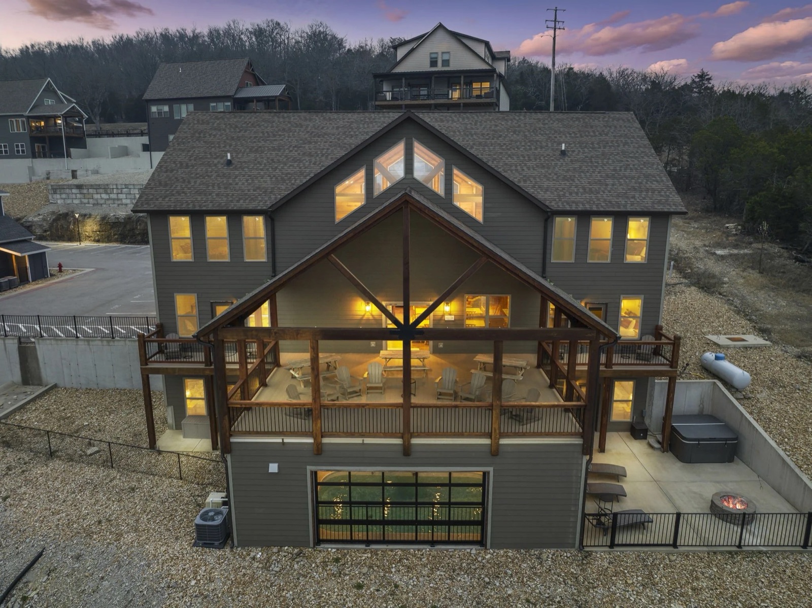 Drone twilight of a luxury three-story Branson STR with glowing windows and hot tub